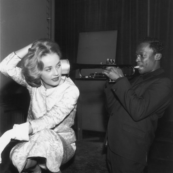 1957:  French actor Jeanne Moreau listens as American jazz musician Miles Davis (1926 - 1991) plays his trumpet, holding it to her ear. There is a mute attached to the bell of the trumpet.  (Photo by RDA/Getty Images)